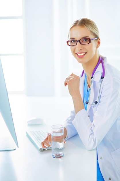 Retrato do jovem médico feminino sentado na mesa no hospital