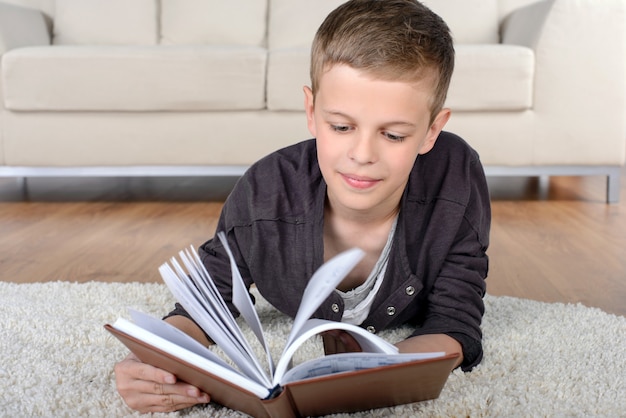 Retrato do livro de leitura inteligente do menino ao encontrar-se no assoalho.