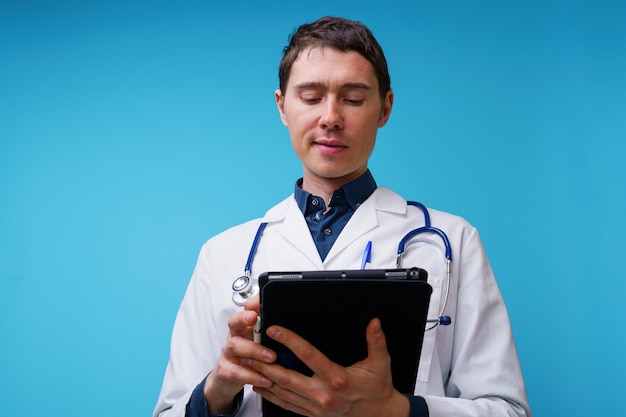 Retrato do médico com estetoscópio e computador tablet na mão sobre fundo azul