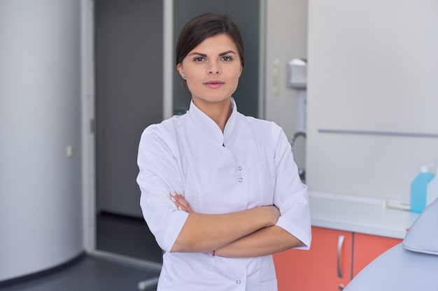 Retrato do médico feminino jovem confiante com os braços cruzados