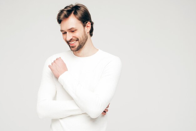 Retrato do modelo de empresário sexual lumbersexual, sorridente, bonito, vestindo calça e suéter branco casual