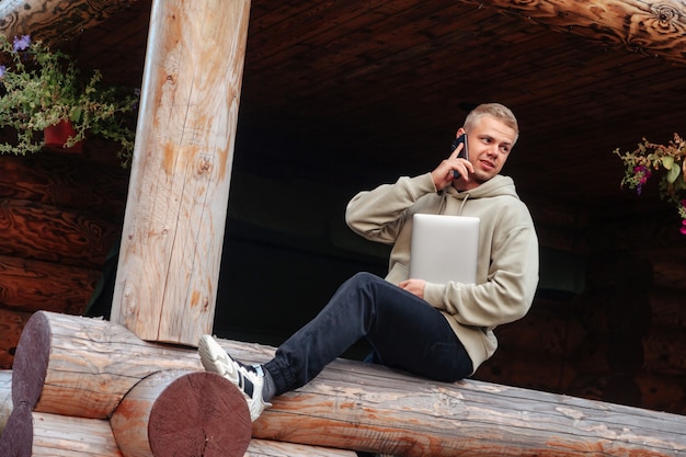 Retrato do moderno empresário jovem com terraço ao ar livre do laptop de casa de campo. homem workaholic em roupas casuais em casa, chamando no telefone. inspiração criativa e negócios de inicialização. copie o espaço