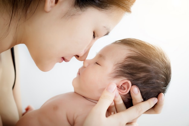 Retrato do nariz pequeno bonito recém-nascido do bebê do nariz asiático feliz do toque do uso da mãe em uma cama branca em casa.