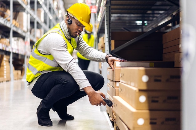 Retrato do pacote de digitalização de homem de engenheiro americano africano com scanner de código de barras verificar mercadorias em transporte e distribuição em armazém. logística industrial e exportação de negócios