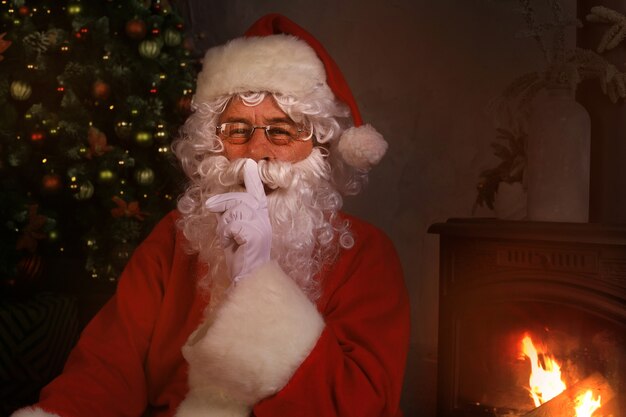 Retrato do Papai Noel mantendo o dedo indicador pela boca e olhando para a câmera.