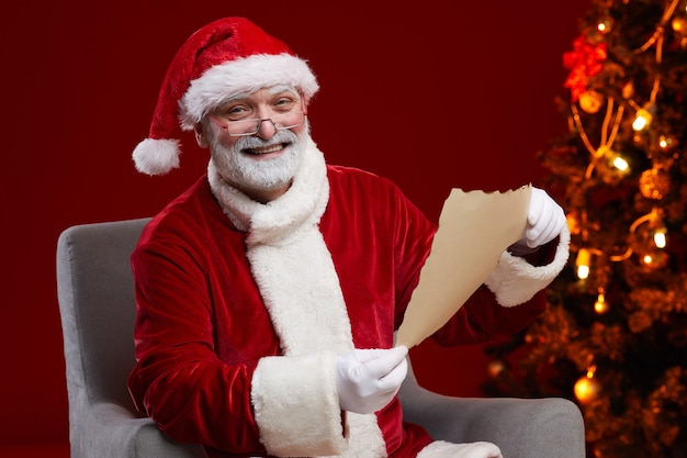 Retrato do Papai Noel sorrindo enquanto está sentado na poltrona e lendo a carta de Natal