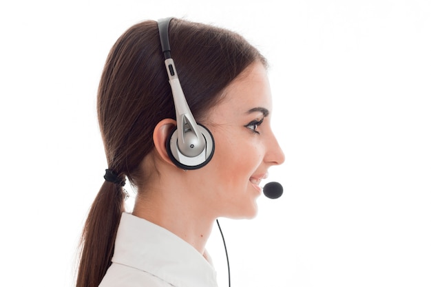 Retrato do perfil da garota morena atraente trabalhadora de call center com fones de ouvido e microfone isolados no fundo branco