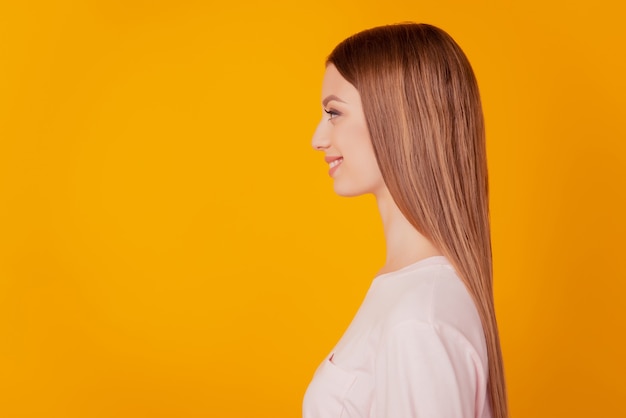 Retrato do perfil da linda senhora positiva olhando para o espaço em branco com um sorriso radiante no fundo amarelo