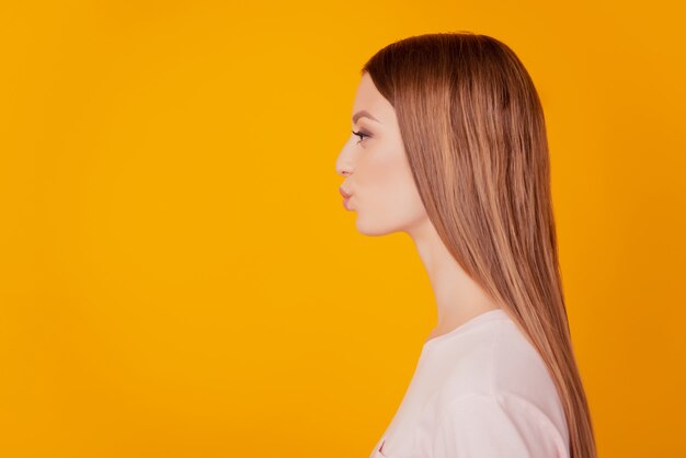 Retrato do perfil da senhora carinhosa e terna olha o espaço em branco lábios enviam beijo no ar sobre fundo amarelo