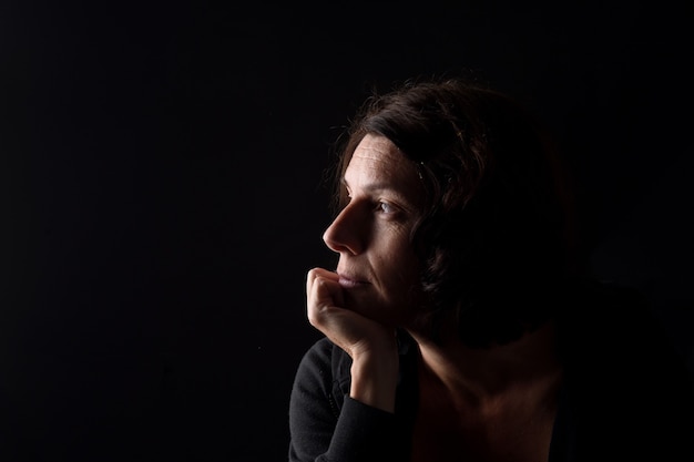 Retrato do perfil de uma mulher séria com a mão no queixo e pensando sobre fundo preto
