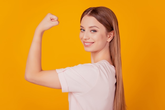 Retrato do perfil de uma senhora charmosa e forte, em forma esportiva, levantando a mão para mostrar os músculos em um fundo amarelo