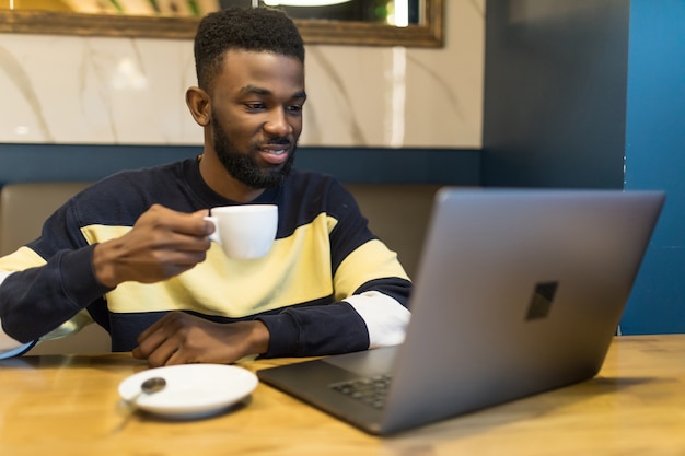 Retrato do perfil do jovem gerente de uma loja da web africana, bebendo um café enquanto trabalhava em um café
