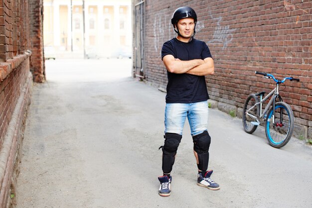 Retrato do piloto ao lado de uma bicicleta no beco do prédio de tijolos vermelhos