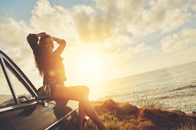 Retrato do pôr do sol de mulher e viagem no capô do carro com sorriso, praia ou felicidade para as férias de verão Menina gen z feliz céu e sol com natureza aventura ao ar livre e férias no oceano em Miami