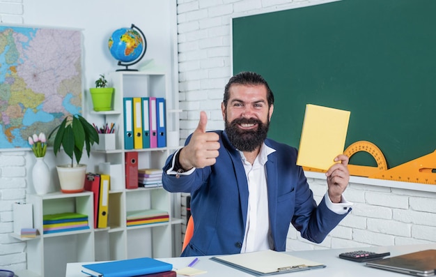 Foto retrato do professor do ensino fundamental masculino com o polegar para cima na sala de aula, sucesso.