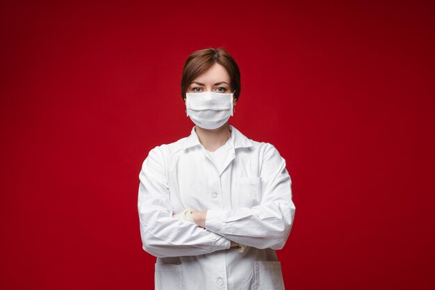 Retrato do profissional médico feminino em uniforme branco e máscara protetora posando isolado