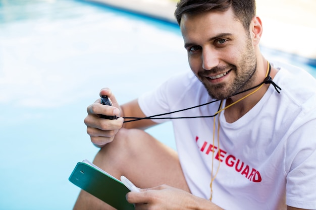 Retrato do salva-vidas segurando a prancheta e o cronômetro à beira da piscina em um dia ensolarado