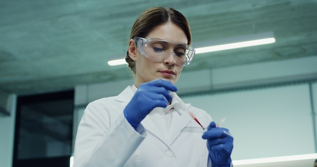 Foto retrato do trabalhador de laboratório feminino bonito caucasiano fazendo um exame de sangue no tubo de vidro nas mãos. fechar-se.