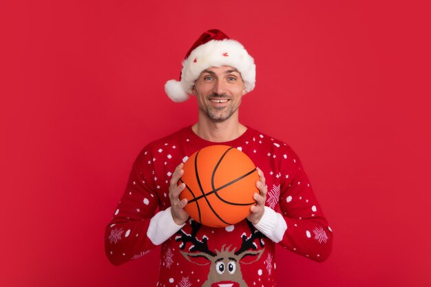 Retrato do treinador de papai noel de natal segura bola de basquete no fundo vermelho do estúdio