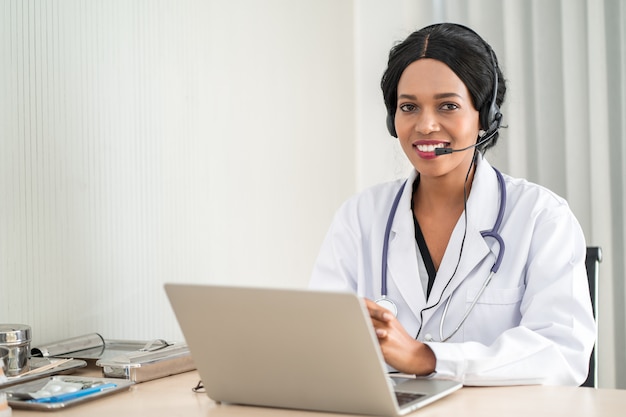 Retrato del doctor joven sonriente feliz afroamericano en auriculares que consulta al paciente por teléfono. Concepto en línea del centro de atención médica