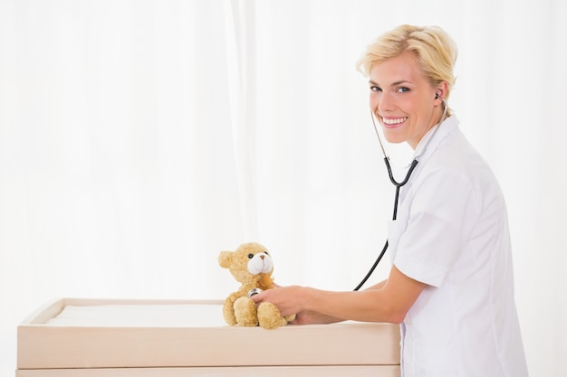 Retrato de un doctor rubio con el estetoscopio y el oso de peluche