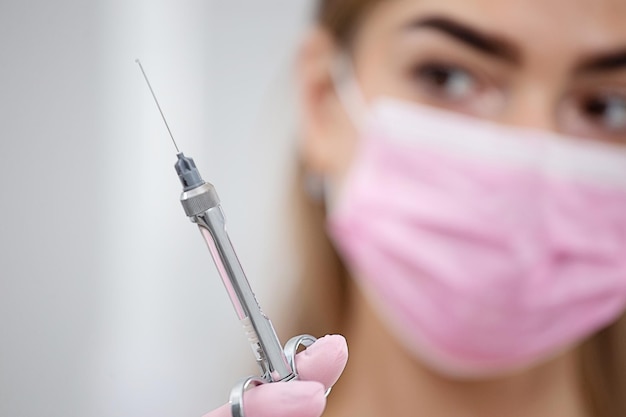 Foto retrato de una doctora con una máscara rosa en la cara con una jeringa en la mano foto borrosa