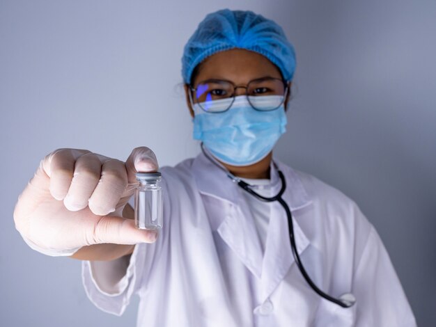 Retrato de una doctora con una máscara y un sombrero Stand sosteniendo una vacuna vacía o un frasco de pastillas.Concepto médico y tratamiento.