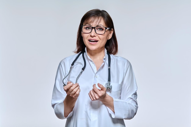 Retrato de una doctora mirando a la cámara hablando gesticulando sobre un fondo claro de estudio