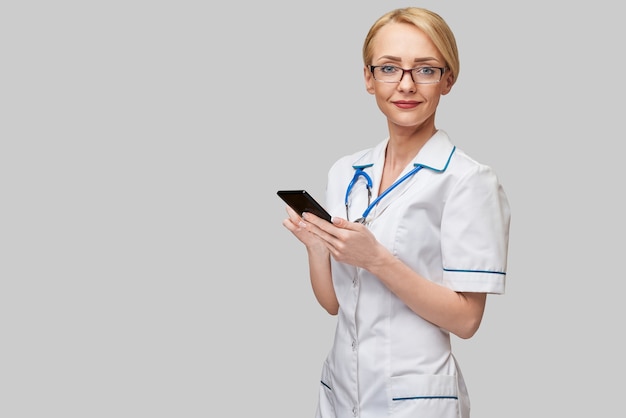 Retrato de una doctora o enfermera sosteniendo y usando un teléfono móvil