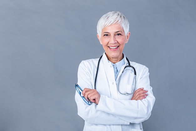 Retrato de doctora senior con estetoscopio y brazo cruzado aislado en la pared