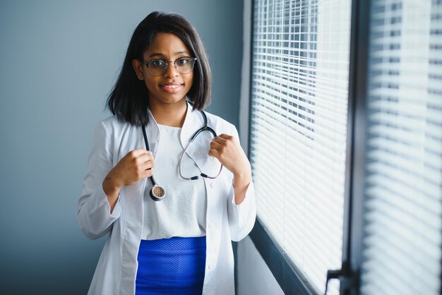 Retrato de una doctora sonriente con bata blanca con estetoscopio en la oficina del hospital