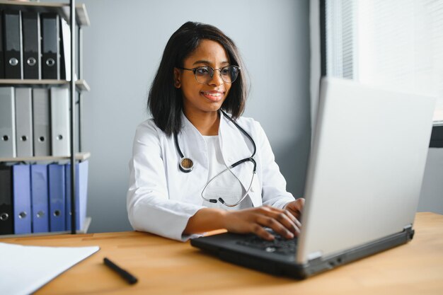 Retrato de una doctora sonriente con bata blanca con estetoscopio en la oficina del hospital