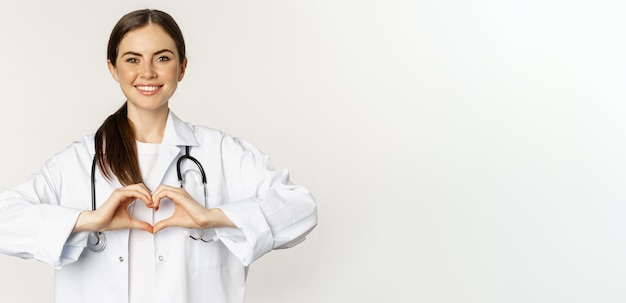 Foto retrato de una doctora sonriente que muestra el signo del corazón y mira con cuidado ama a su paciente