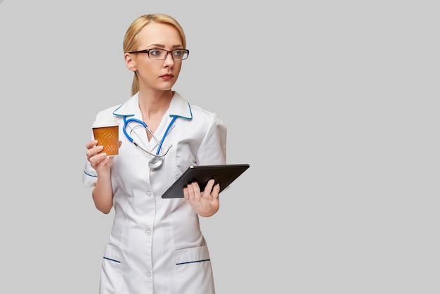 Retrato de una doctora sosteniendo una taza de café de papel y sosteniendo la almohadilla de la tableta