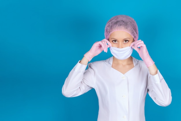 Retrato de una doctora en uniforme médico con una máscara protectora Aislar sobre una superficie azul