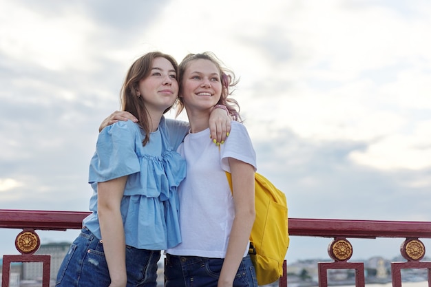 Retrato de dos adolescentes de pie en el puente sobre el río, amigos caminan en un día soleado de verano. Amistad, estilo de vida, juventud, adolescentes