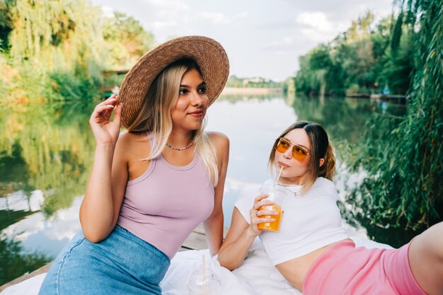 Retrato de dos amigas alegres descansando al aire libre en el muelle del lago.