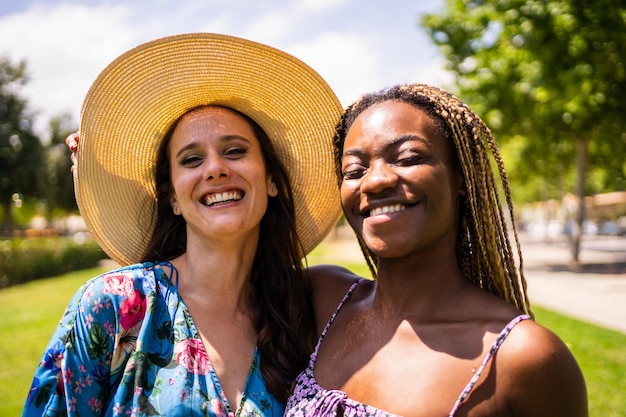 Retrato de dos amigos multiétnicos sonriendo a la cámara en traje de verano en un jardín.