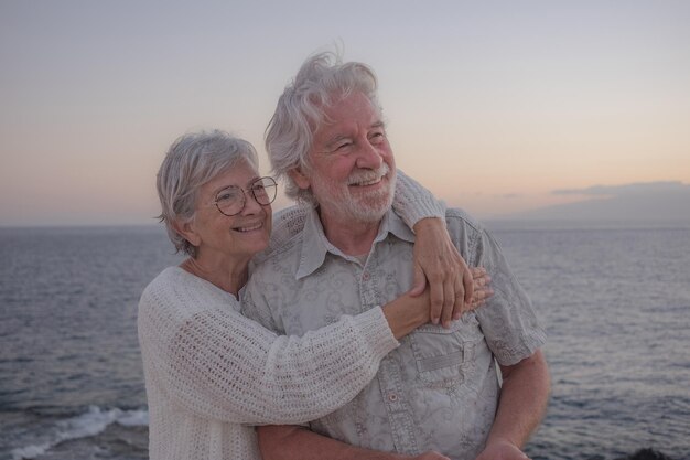 Retrato de dos ancianos felices y románticos o jubilados abrazados en el mar a la luz del atardecer vieja pareja senior sonriente al aire libre disfrutando de las vacaciones juntos