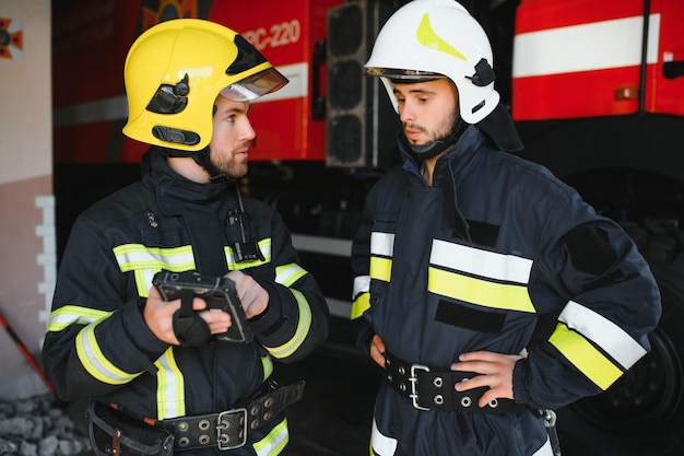 Retrato de dos bomberos en la operación de extinción de incendios bombero con ropa protectora y casco usando una tableta en acción luchando