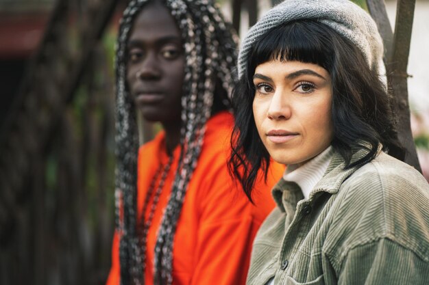 Retrato de dos chicas de 20 años de diferentes razas mientras se sientan al aire libre mirando el concepto de amistad e integración de la cámara