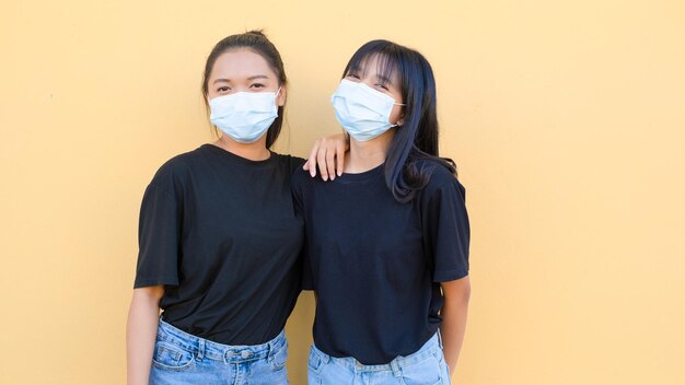 Retrato de dos chicas jóvenes que usan máscaras de pie juntas en un backgroynd naranja.