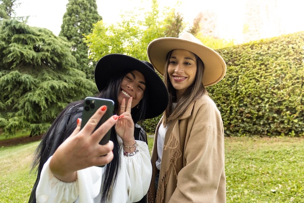 Retrato de dos chicas sonrientes con sombreros tomándose una selfie Cerca de dos amigas con sombreros tomándose una selfie al aire libre