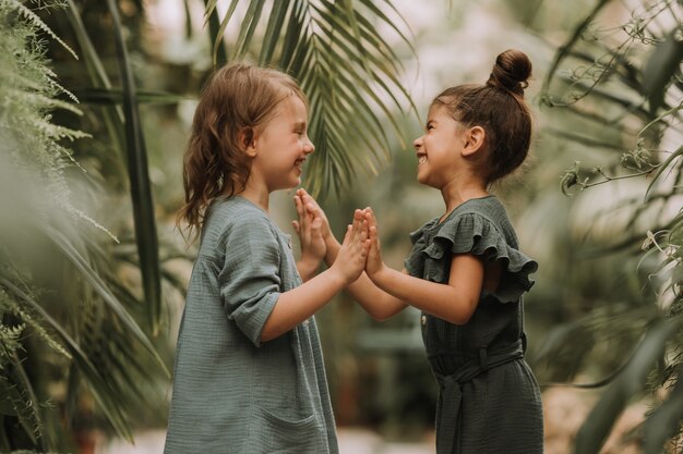 Retrato de dos encantadoras niñas sonrientes pertenecientes a diferentes razas rodeadas de hojas tropicales