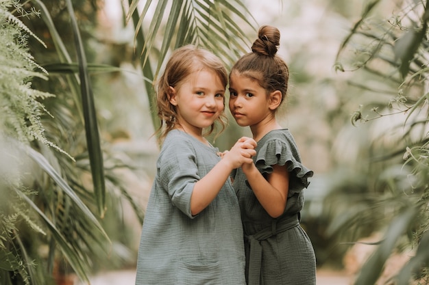 Retrato de dos encantadoras niñas sonrientes pertenecientes a diferentes razas rodeadas de hojas tropicales