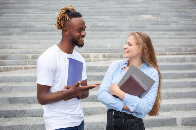 Retrato de dos estudiantes multiétnicos sonrientes con caras felices posando al aire libre