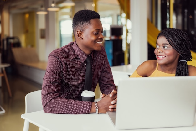 Retrato de dos estudiantes negros con netbook sentados en el interior de la casa, afroamericanos usando una computadora portátil para buscar información y hacer reservas