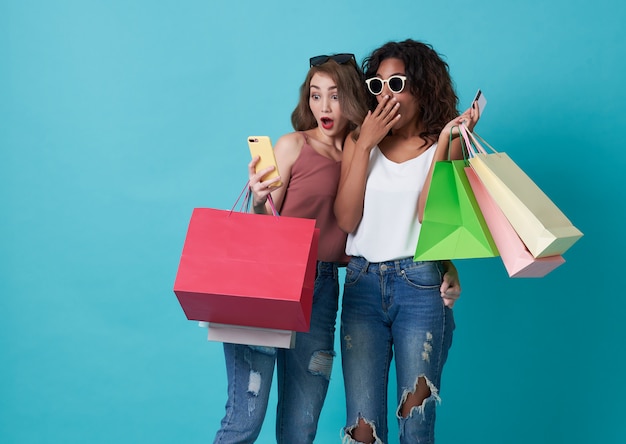 El retrato de dos excitó la mano de la mujer joven que sostenía el teléfono móvil y el bolso de compras aislado sobre fondo azul.