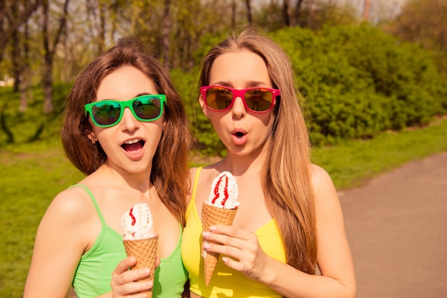 Retrato de dos hermanas conmocionadas en vasos comiendo helado