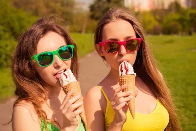 Retrato de dos hermanas jóvenes en vasos comiendo helado